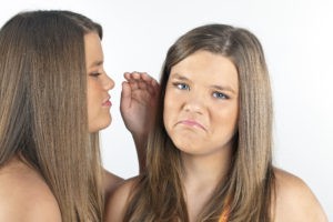 Twin sisters telling secrets to each other in a studio environment on a white background